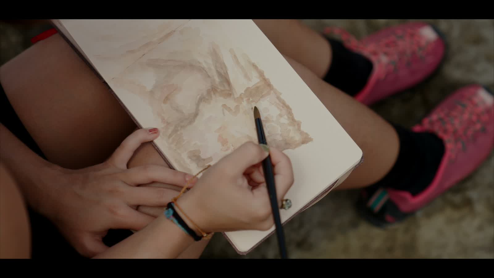 Las manos de Marcela pintando la pared en un cuaderno, con un pincel